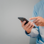 Homem de camisa azul usando smartphone com a mão.